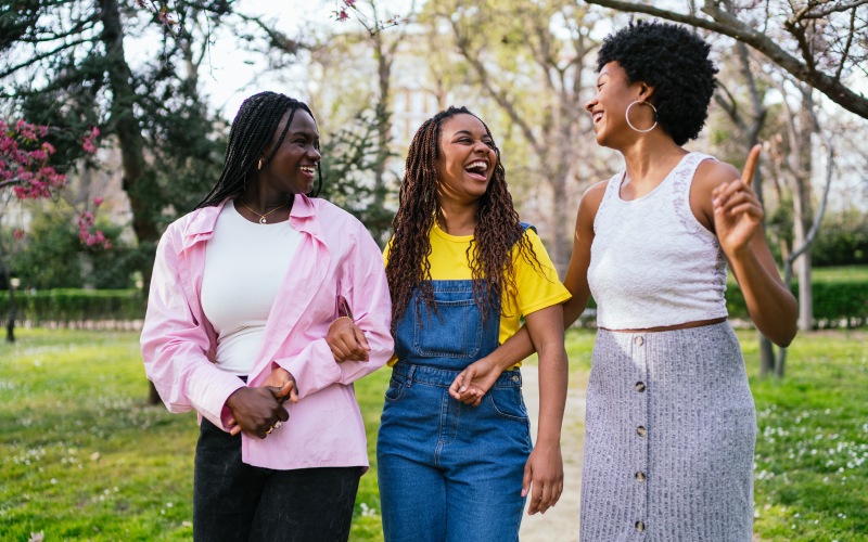 three friends laughing and walking through park